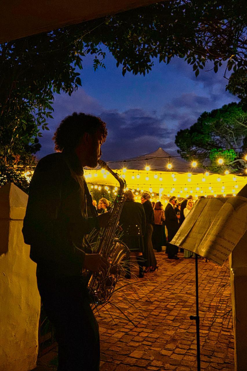 Saxophonist performing at an evening event under string lights